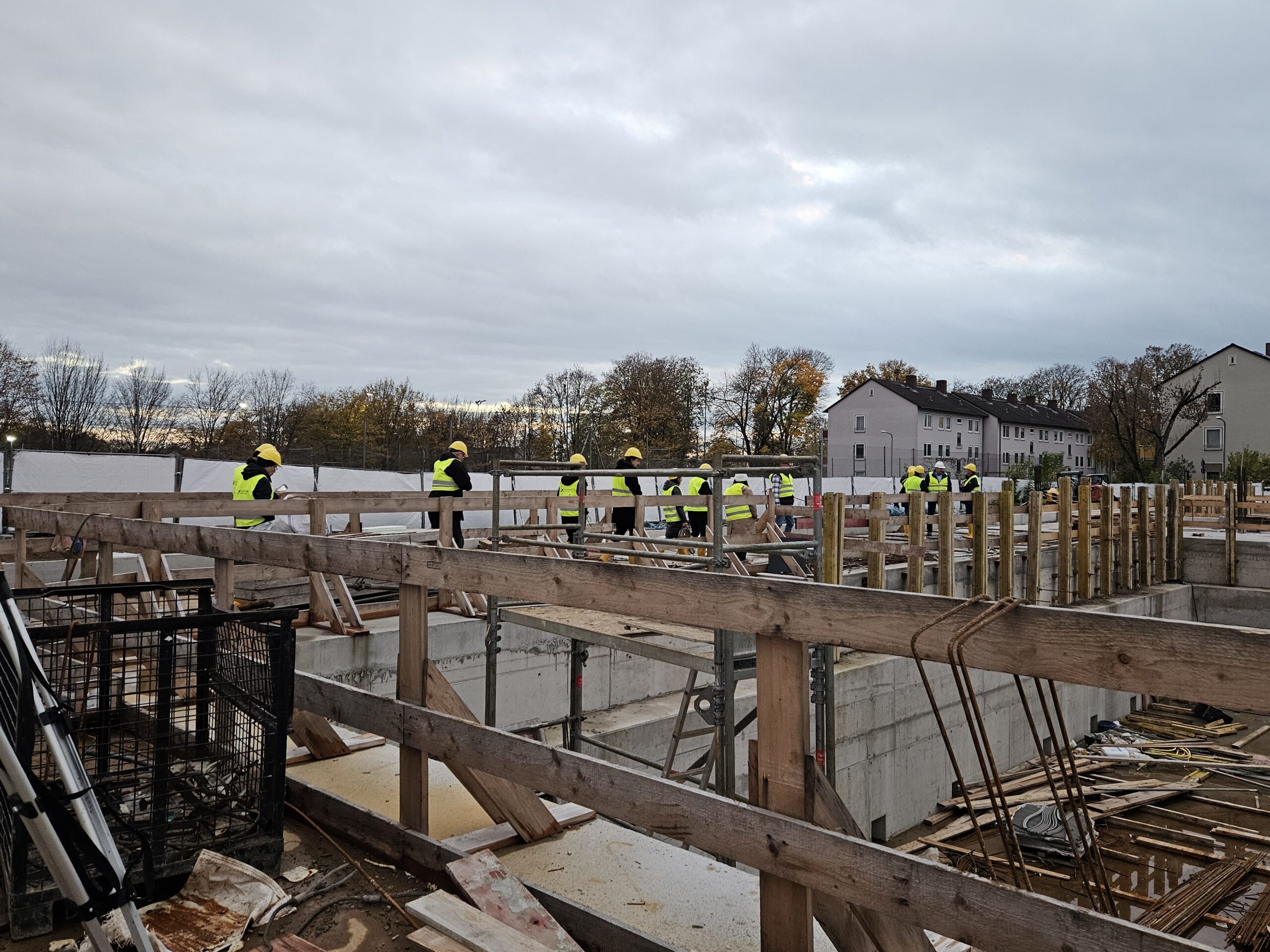 Mehrere Personen mit gelben Sicherheitshelmen und Warnwesten stehen auf einer großen Baustelle.